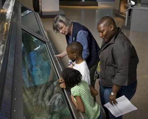 A museum volunteer shows two kids and their mother the giant squid.