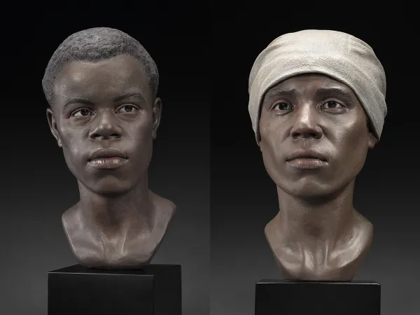 Realistic sculptures of two faces of African descent, one male and one female. The female is wearing a beige head scarf.