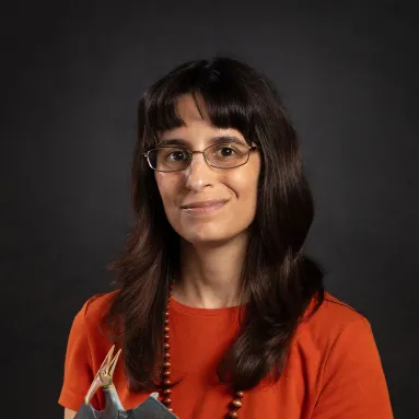image of woman with long dark hair wearing glasses and red shirt holding toy pteranodon